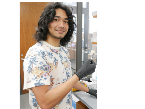 Profile image of Vivian Rogers, sitting on grass in front of a lake/fountain, full body.