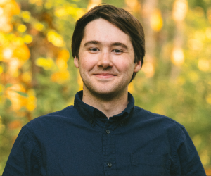 zachary Profile image of Vivian Rogers, sitting on grass in front of a lake/fountain, full body.